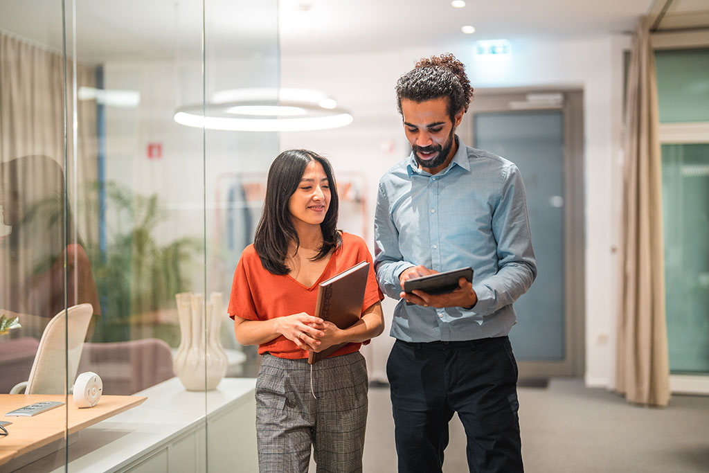 Collaborative - image of employees walking through office whil looking at a tablet